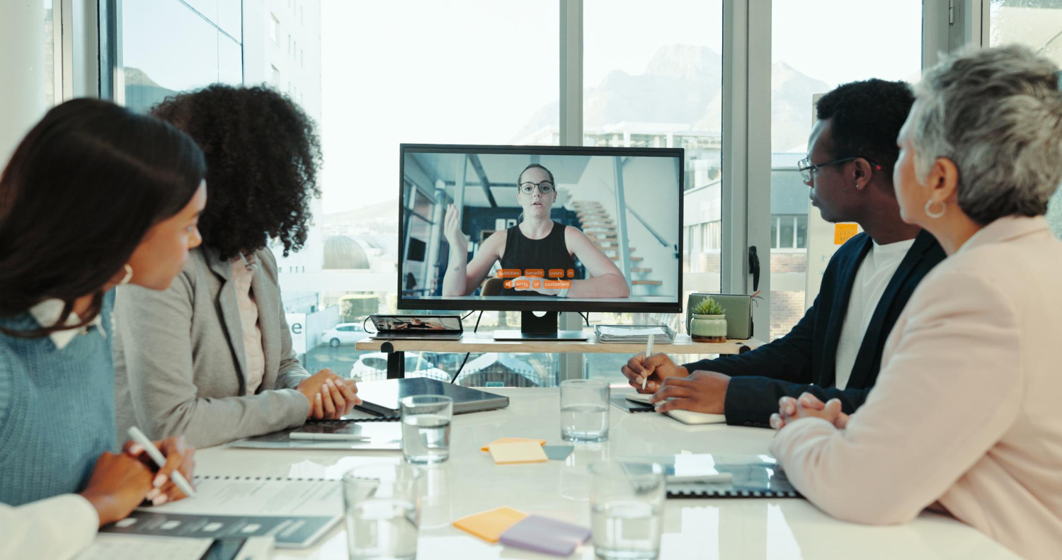 4 people sat in a business meeting watching a video that has subtitles